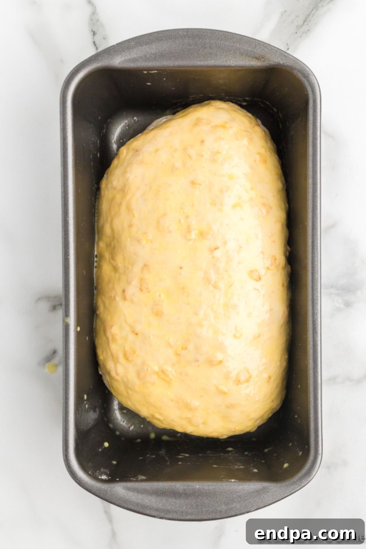 Oatmeal bread dough shaped in a loaf pan with oat topping.