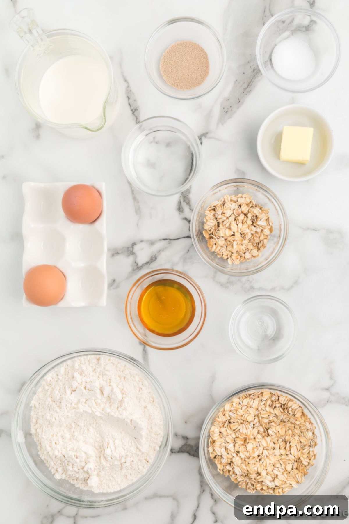 A collection of oatmeal bread ingredients including rolled oats, butter, milk, and yeast on a kitchen counter.