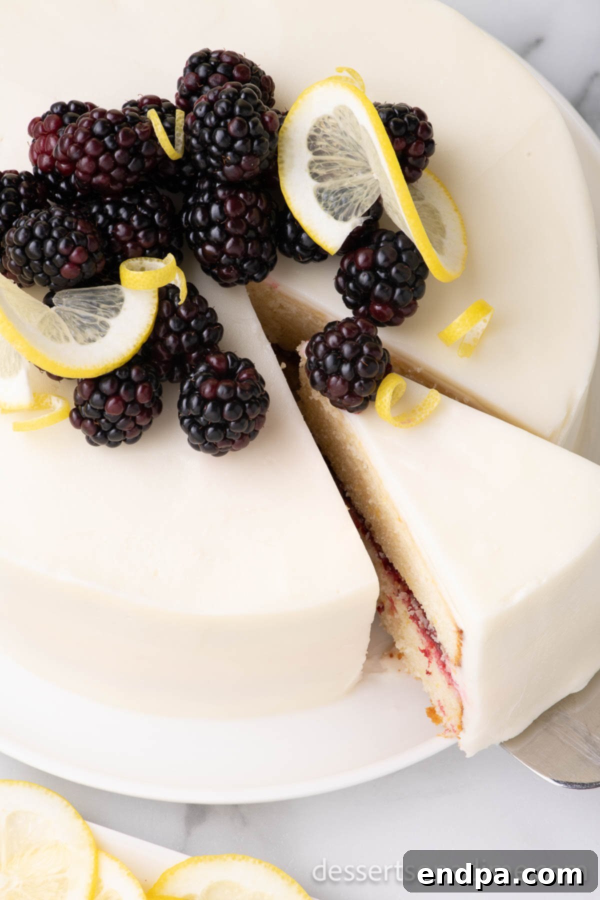 Luscious Lemon Blackberry Cake 2 A freshly sliced Lemon Blackberry Cake, revealing its beautiful layers of lemon cake and vibrant blackberry filling, topped with lemon buttercream and fresh berries.