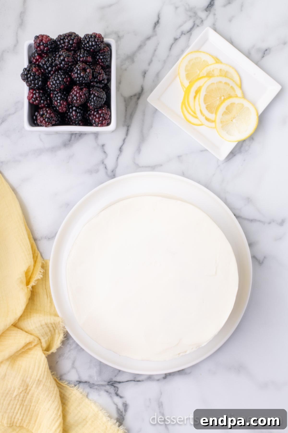 Luscious Lemon Blackberry Cake 13 A two-layer cake being frosted with lemon buttercream, starting with a thin crumb coat.