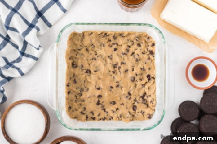 Ultimate Decadence Cheesecake Bars 4 Chocolate chip cookie dough pressed into the bottom of a baking dish, ready for baking.