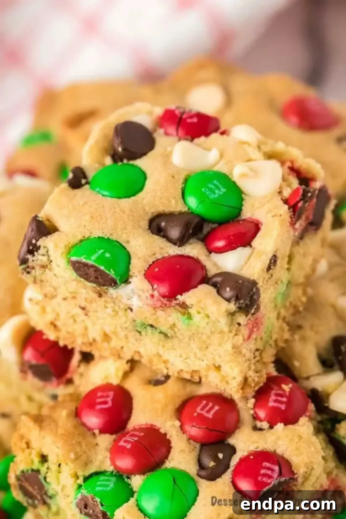 Delicious Christmas Cookie Bars stacked, showcasing the blend of chocolate chips and M&M's. Stacked Christmas Cookie Bars with visible M&M's and chocolate chips, showcasing their gooey texture.