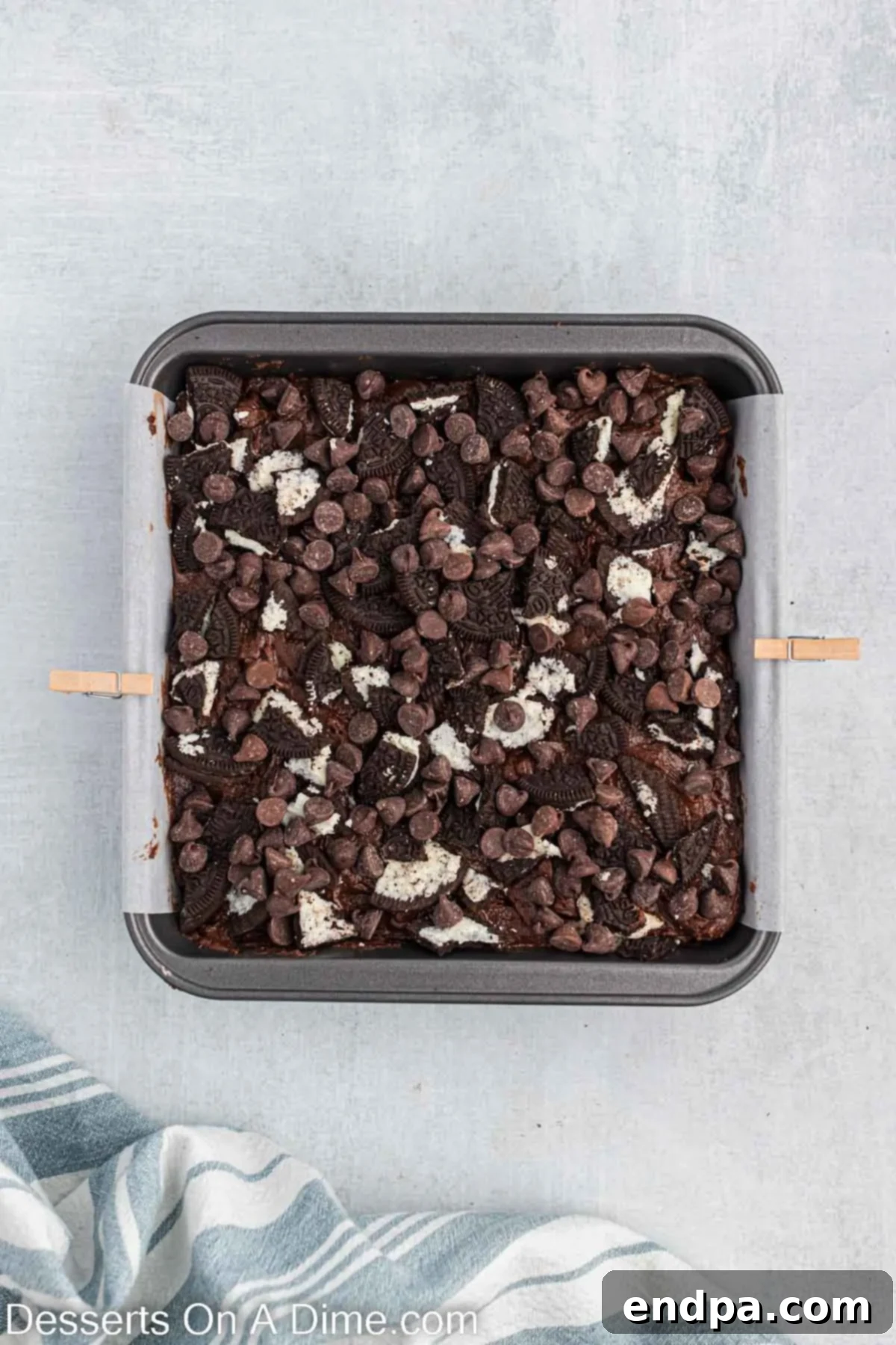 Remaining brownie batter poured over the Oreo layer, topped with crushed cookies and additional chocolate chips.