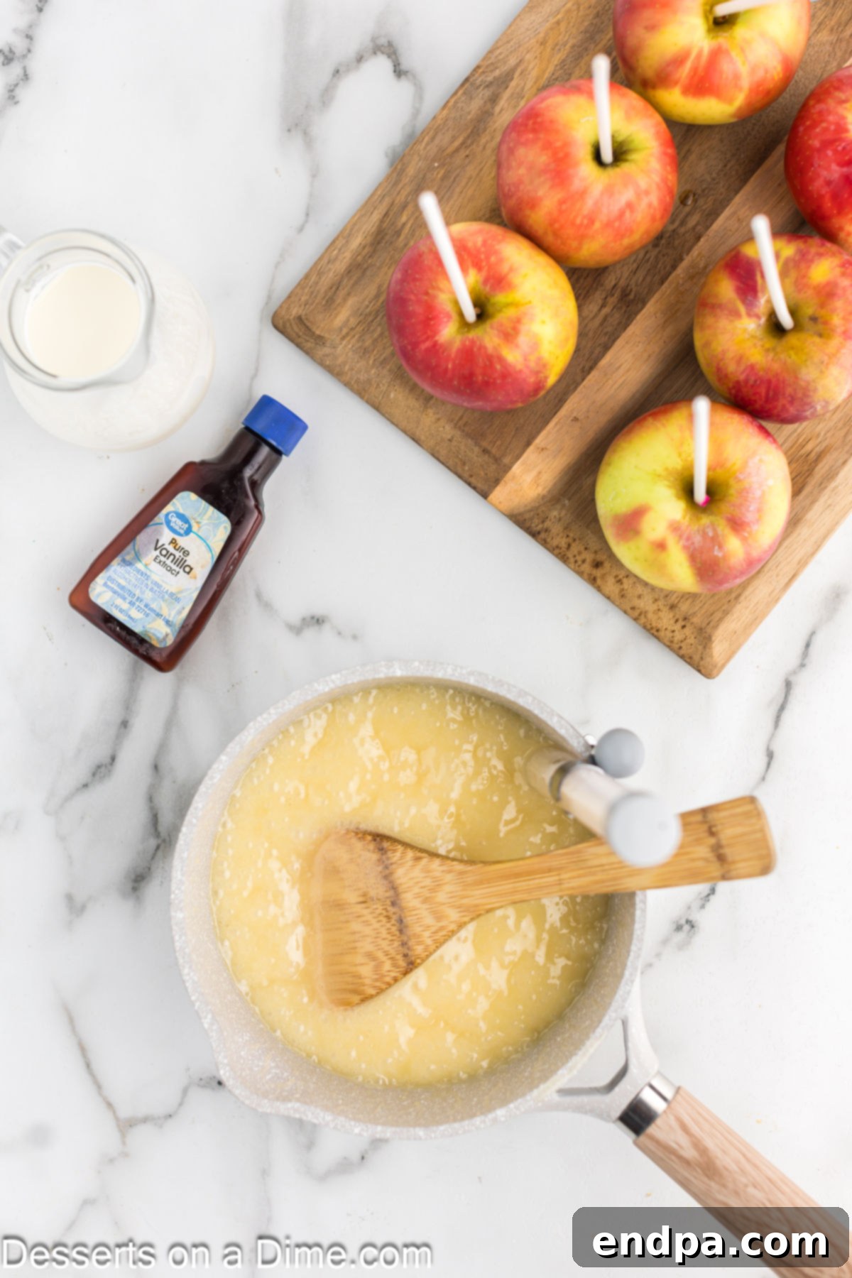 A saucepan on a stovetop, containing a simmering mixture of heavy cream, corn syrup, butter, and sugar, being stirred with a wooden spoon.