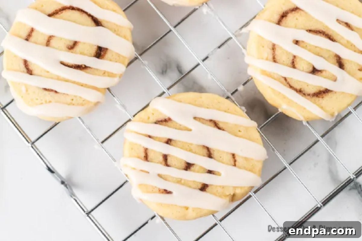 Baked cinnamon roll cookies with icing cooling on a wire rack.