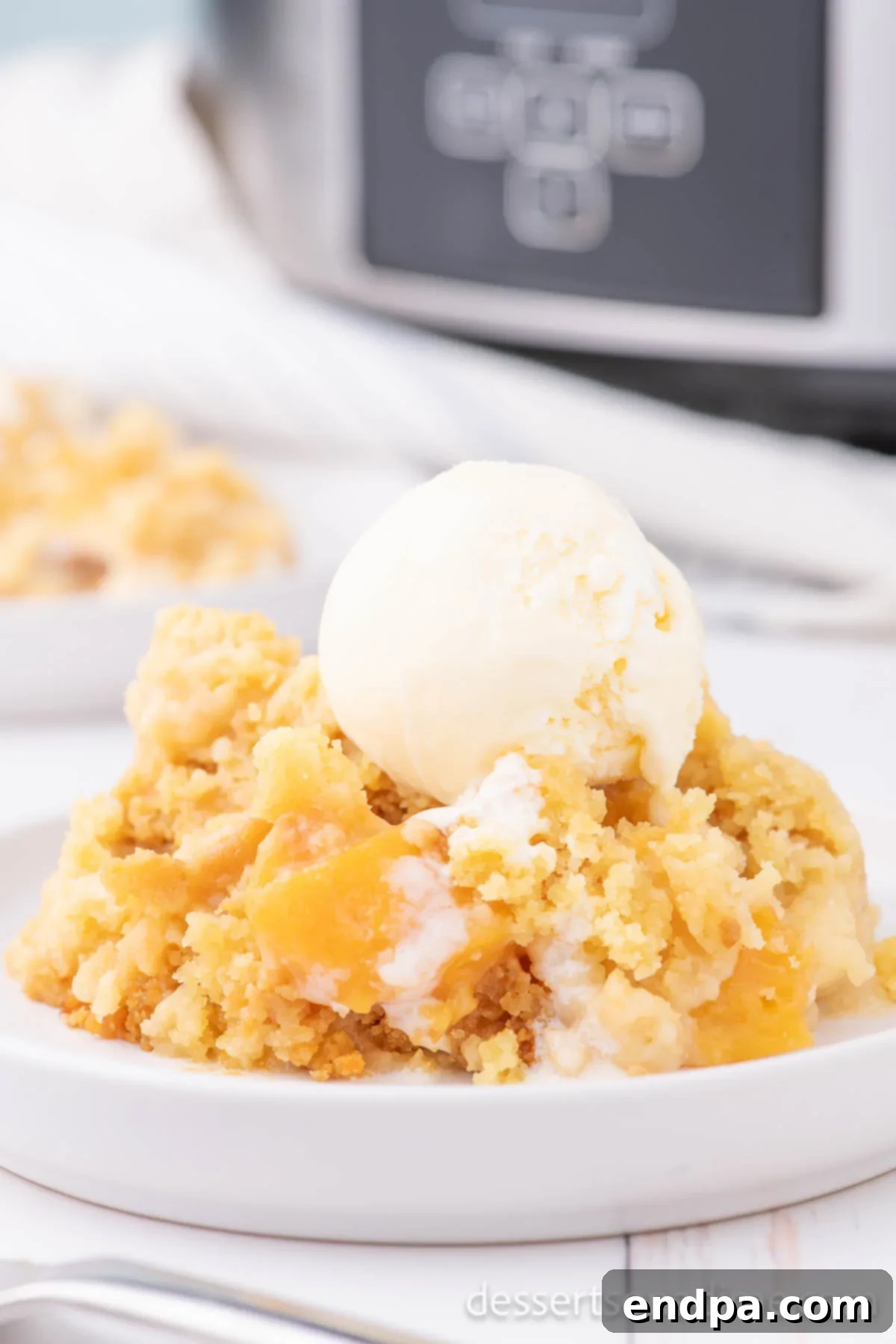 A delectable bowl of Crock Pot Peach Dump Cake, generously topped with a scoop of creamy vanilla ice cream, ready to be enjoyed.