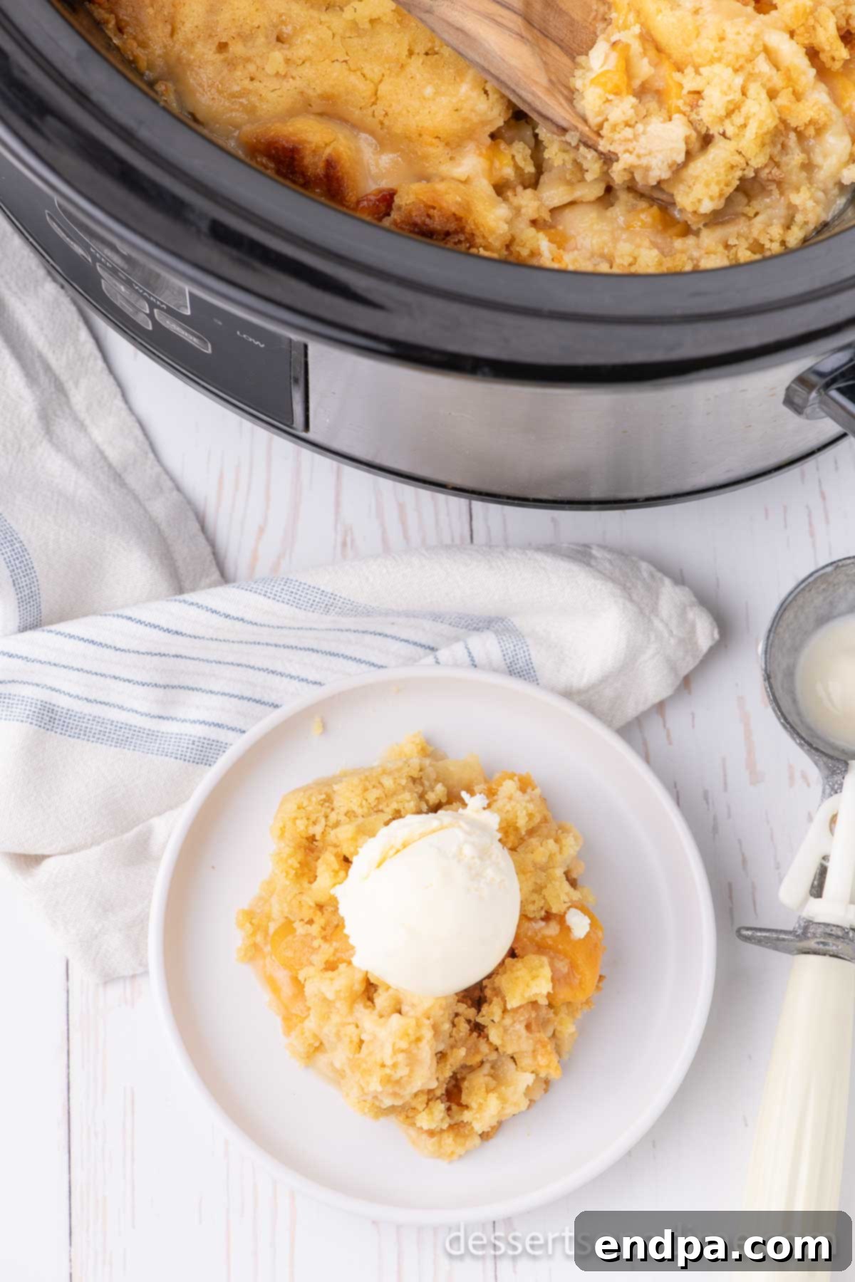 A close-up of a serving of Peach Dump Cake, topped with a generous scoop of vanilla ice cream, capturing the golden-brown cake and juicy peaches beneath.
