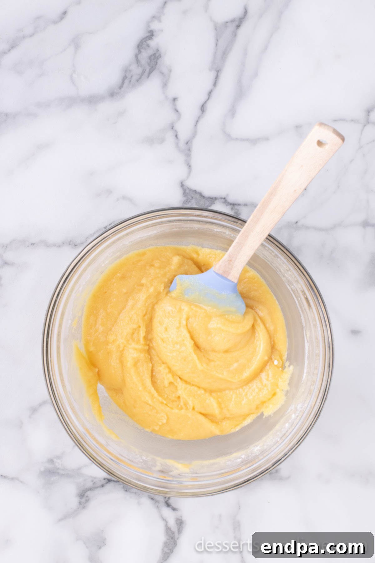 Melted butter is being poured into the mixing bowl containing the dry cake mix, creating a crumbly texture.
