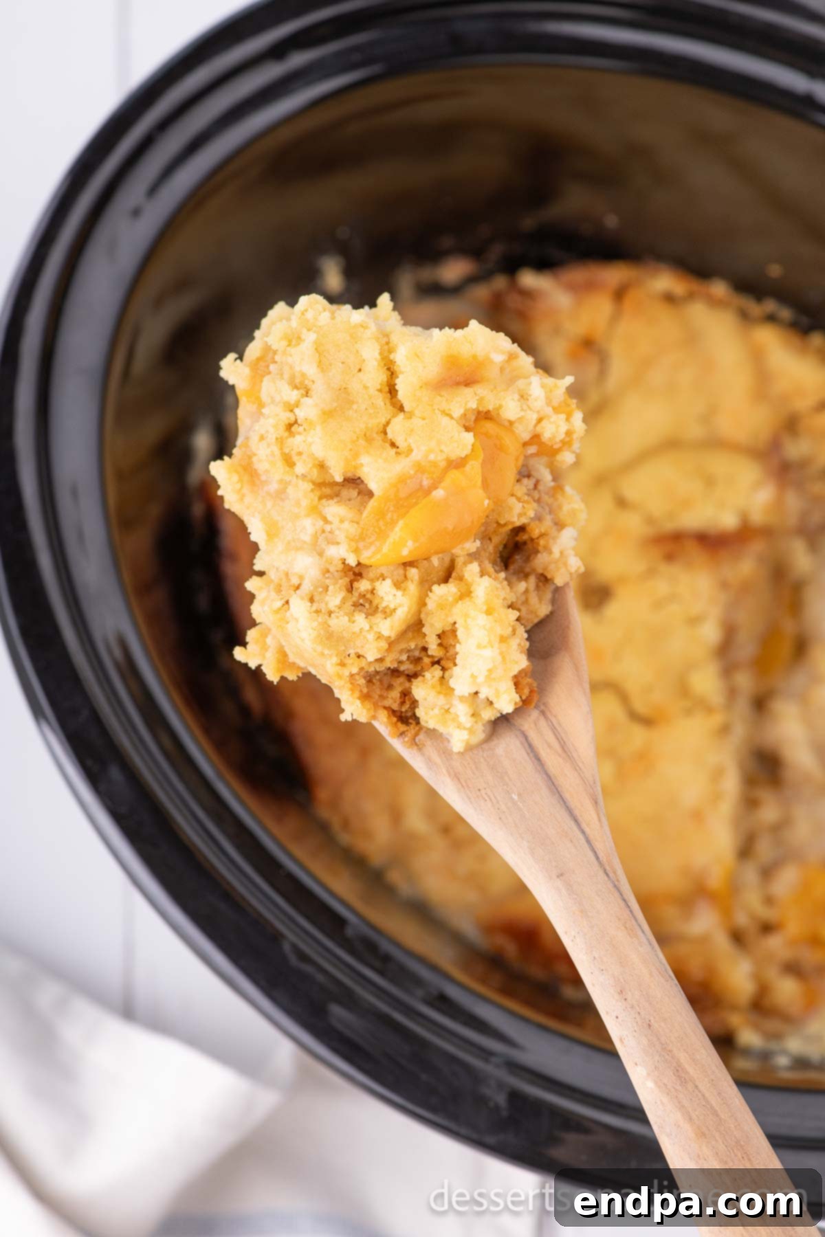 A serving of Crock Pot Peach Dump Cake being scooped out of the slow cooker, steam gently rising, indicating its warmth and readiness.