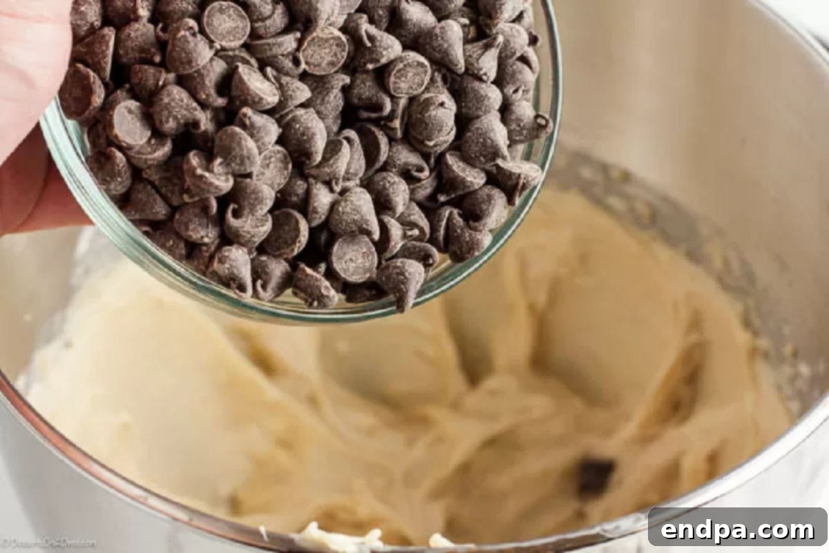 Mini chocolate chips being gently folded into the creamy cookie dough dip mixture with a spatula.