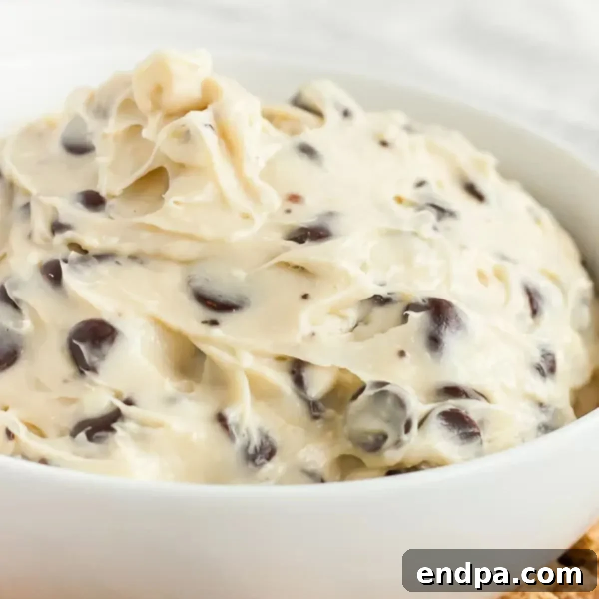 A close-up of a serving bowl filled with creamy chocolate chip cookie dough dip.