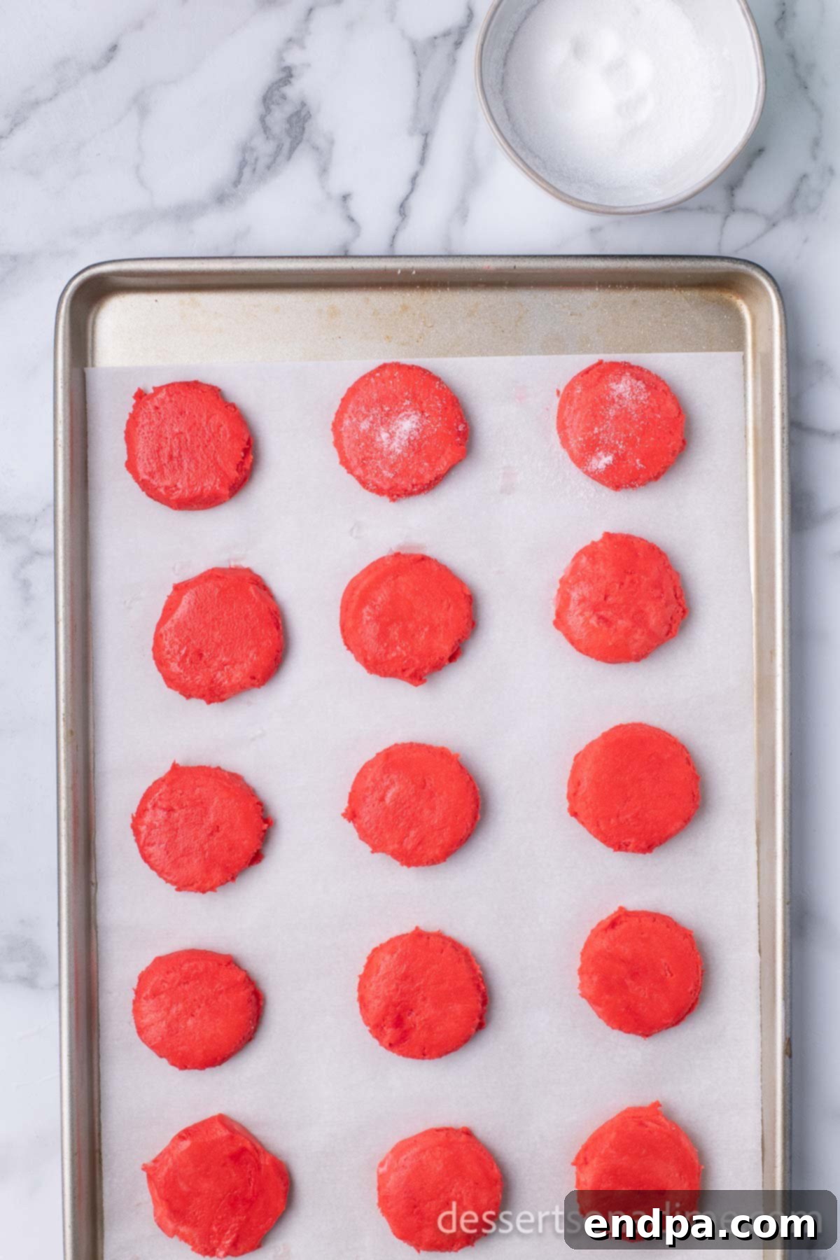 Dark Chocolate-Dipped Peppermint Cookie Delights 9 Flattened cookie dough on a baking sheet, lightly sprinkled with sugar.