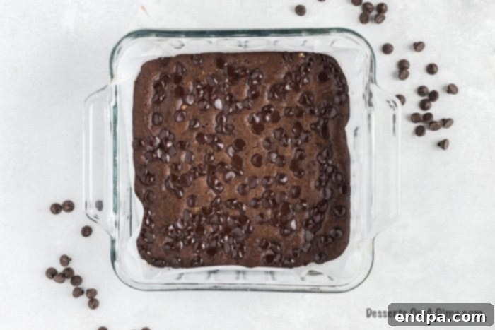 Irresistible Keto Chocolate Fudgies 3 Keto brownie batter smoothly poured into a parchment-lined baking dish, ready for chocolate chips.