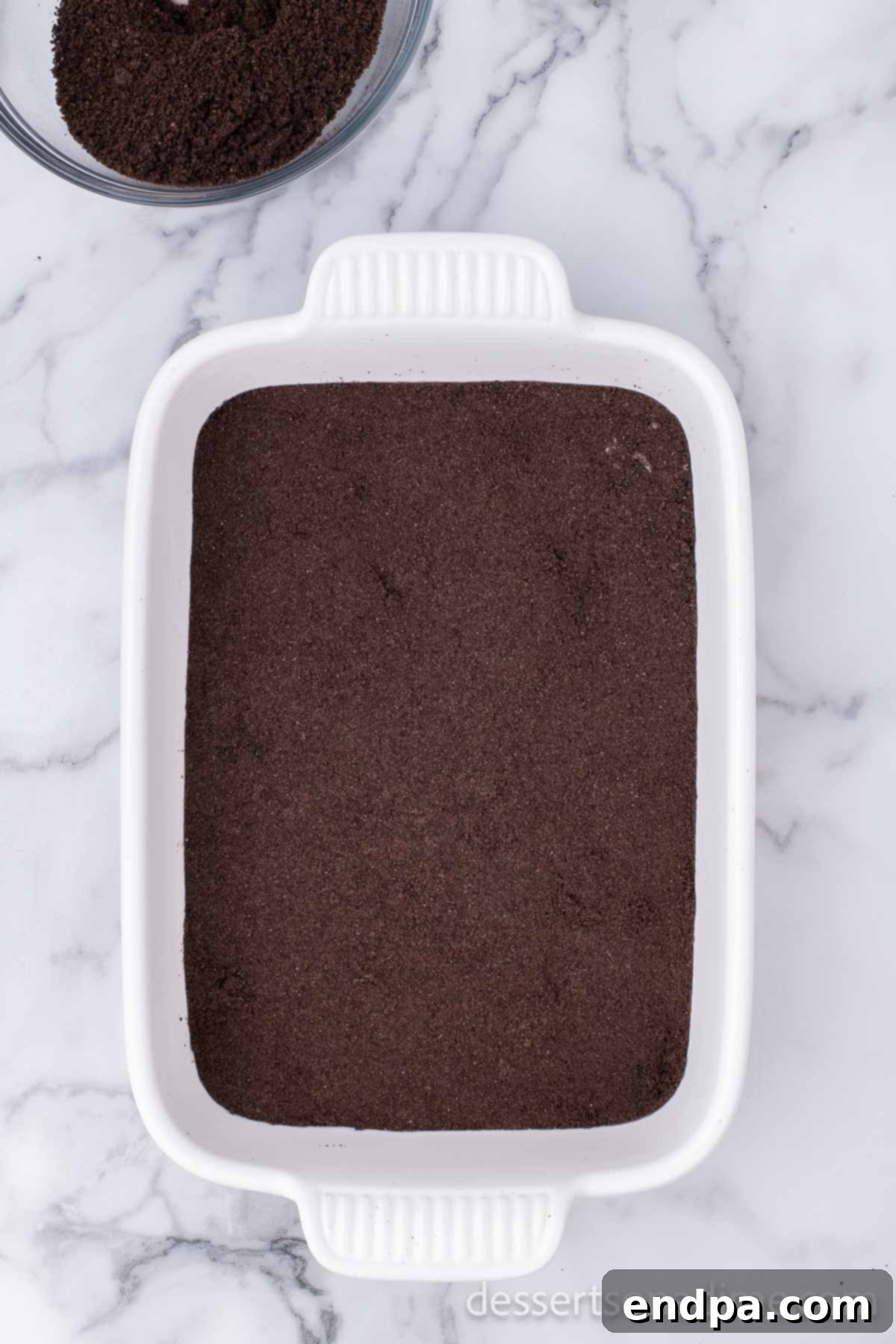 Crushed Oreo cookies form the base layer in a 9x13 baking dish.