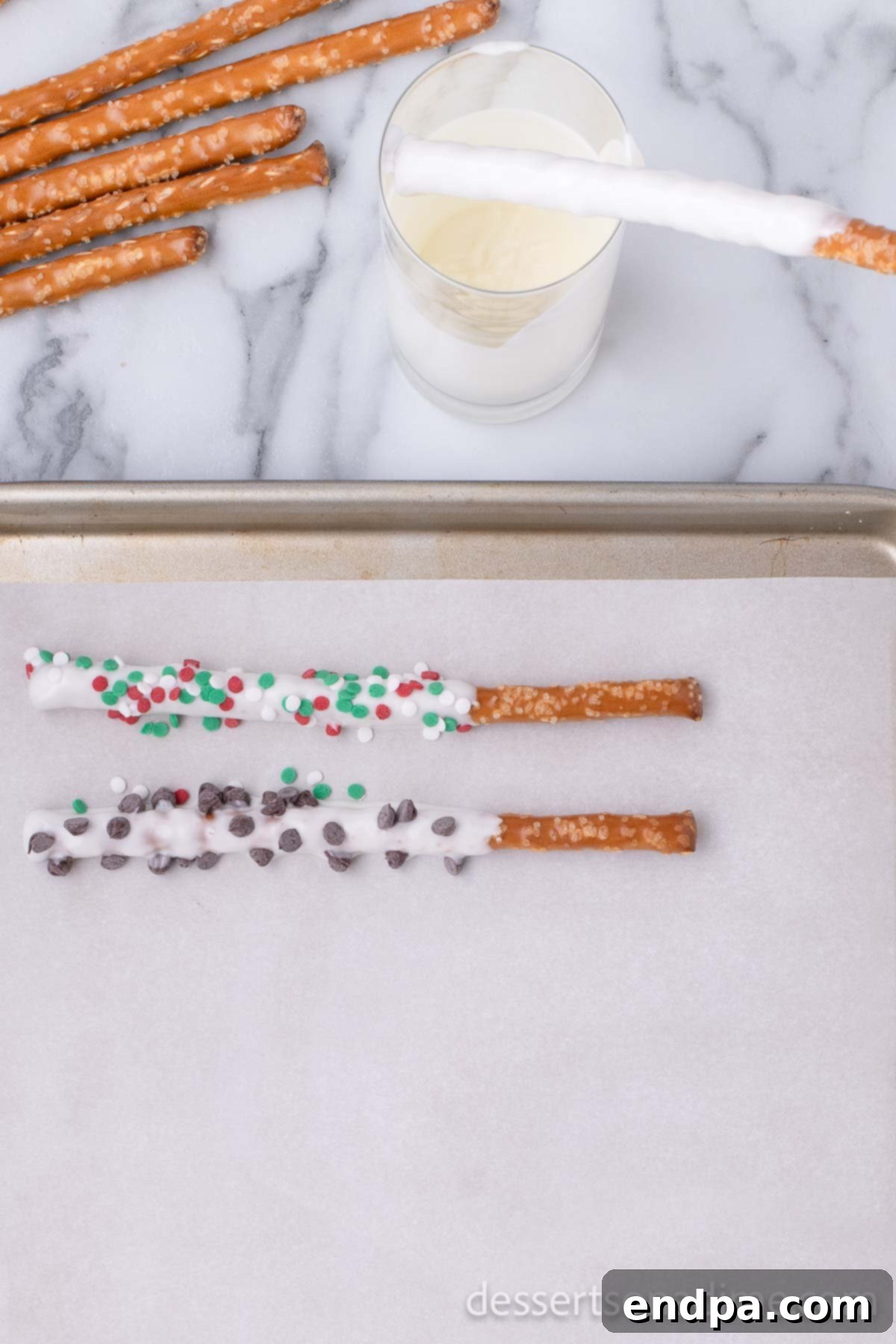 Pretzel rods freshly dipped in melted white chocolate and dark chocolate, laid out carefully on a parchment-lined baking sheet to set.