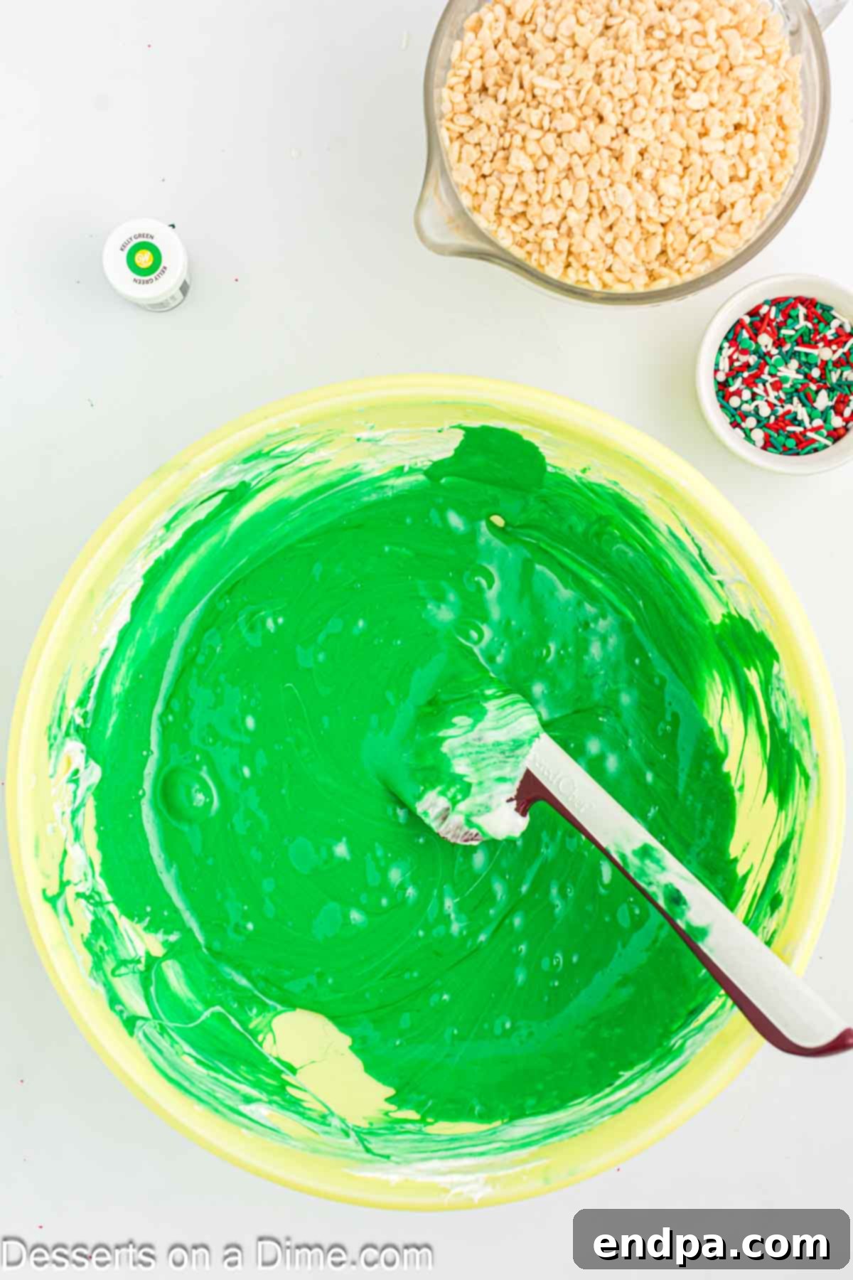 Mixing bowl with melted marshmallows and green food coloring, stirring to combine.