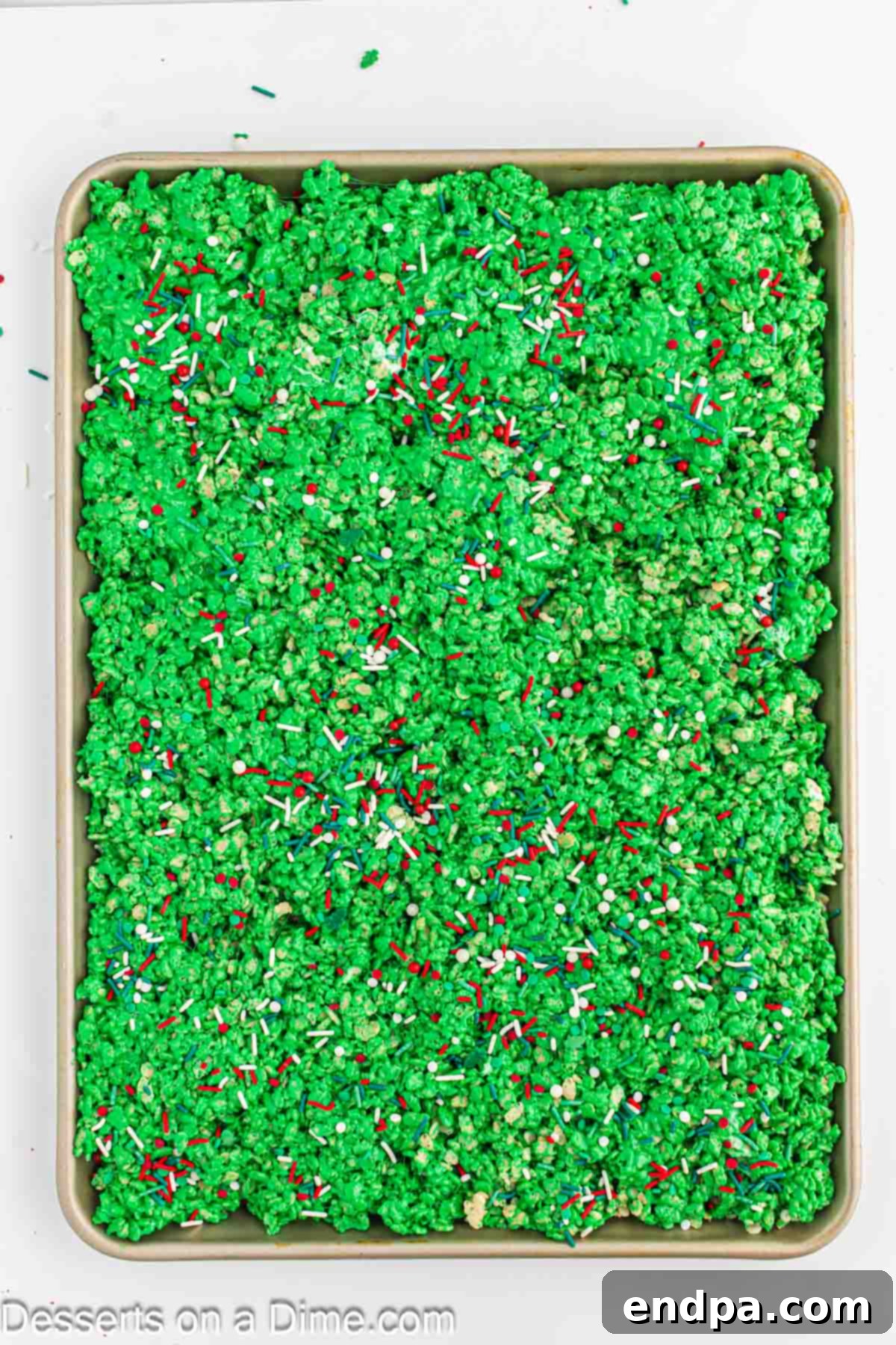 The green cereal mixture pressed evenly into a pan and topped generously with colorful Christmas sprinkles.
