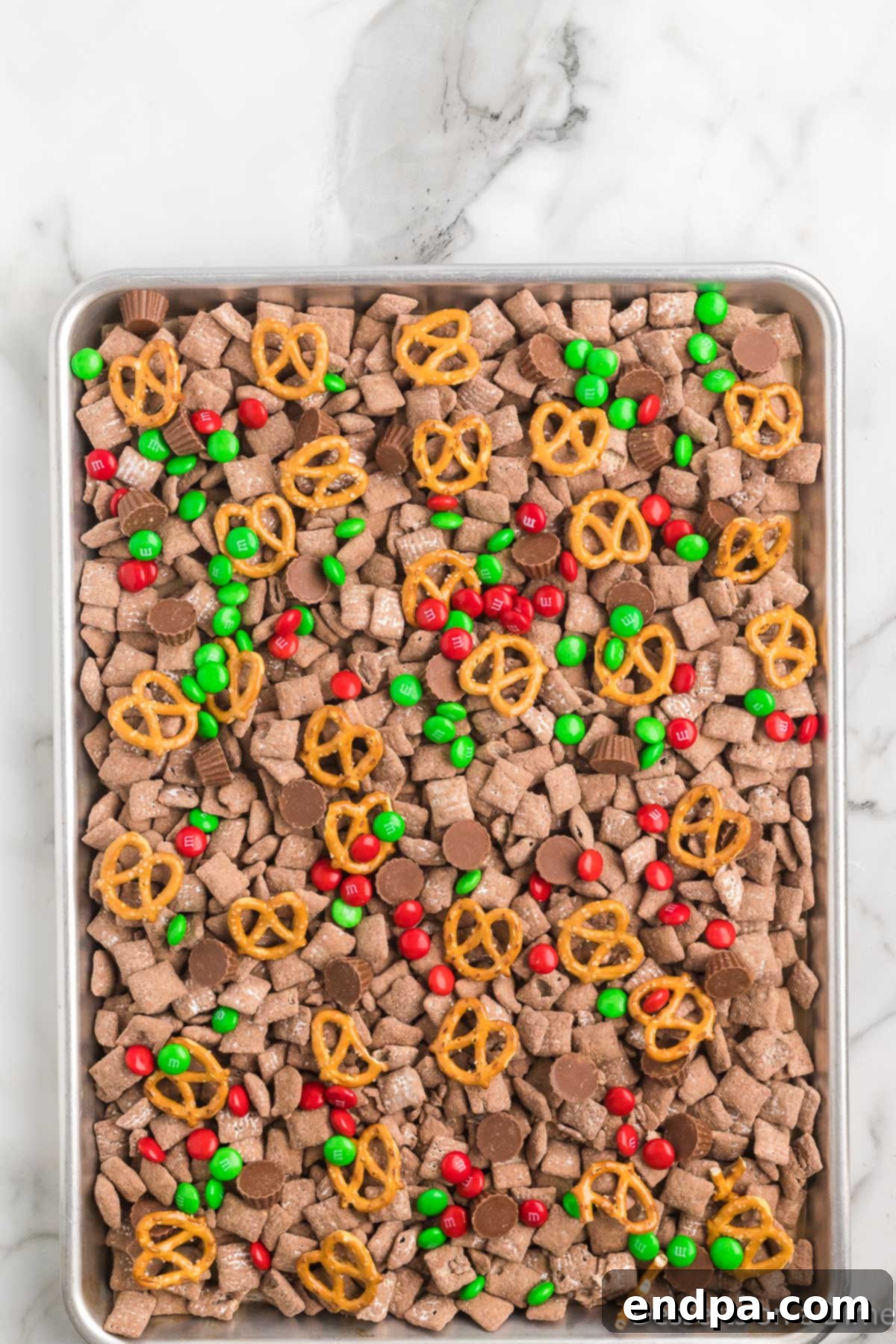 Sheet pan filled with finished Reindeer Chow, including M&M's, peanut butter cups, and pretzels.