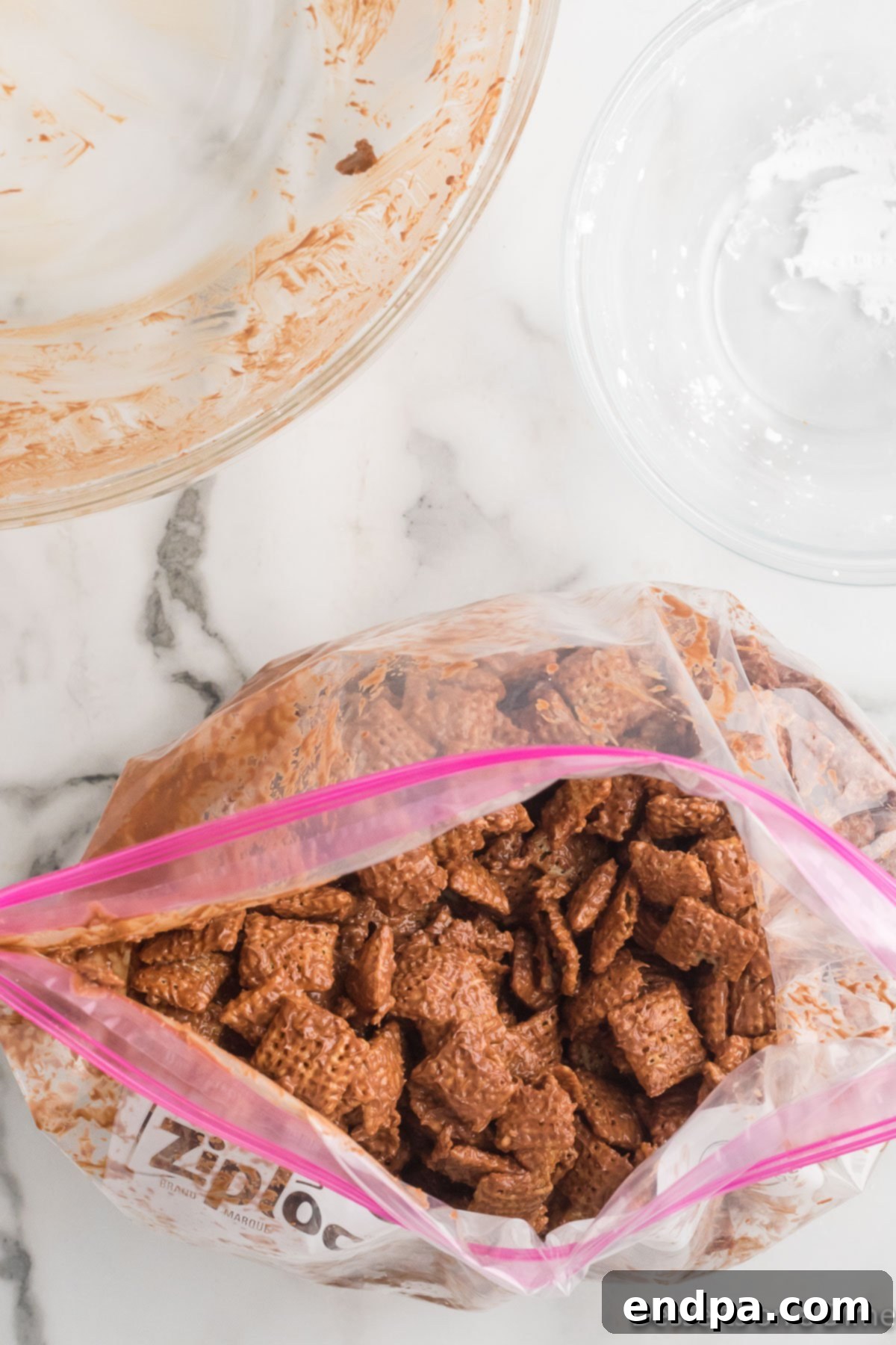 Chocolate-coated cereal being poured into a ziplock bag with powdered sugar.