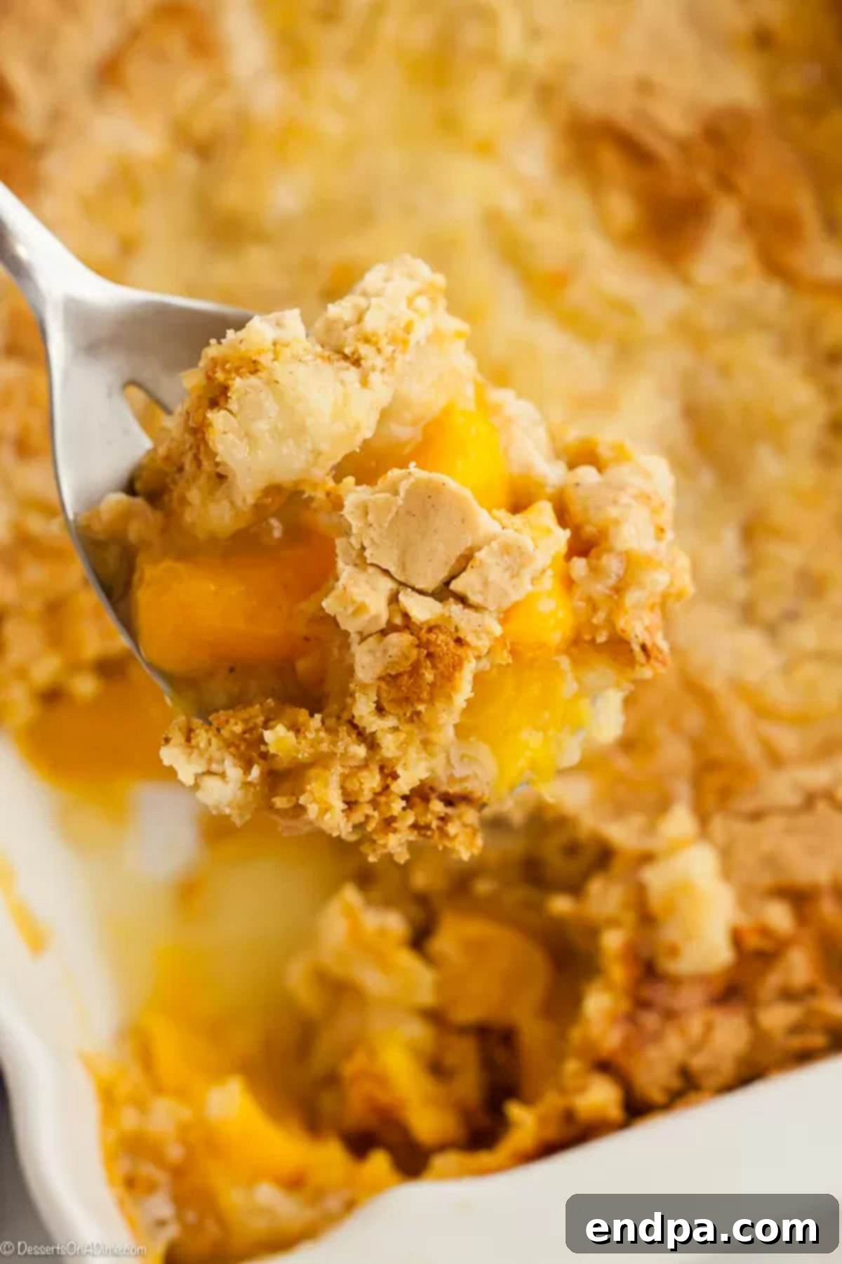 Cobbler dish of peach dump cake with a serving spoon, highlighting the golden crust and bubbling fruit.