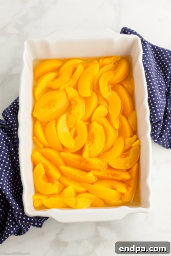 Sliced peaches with syrup in a glass baking dish, forming the base layer of the dump cake.