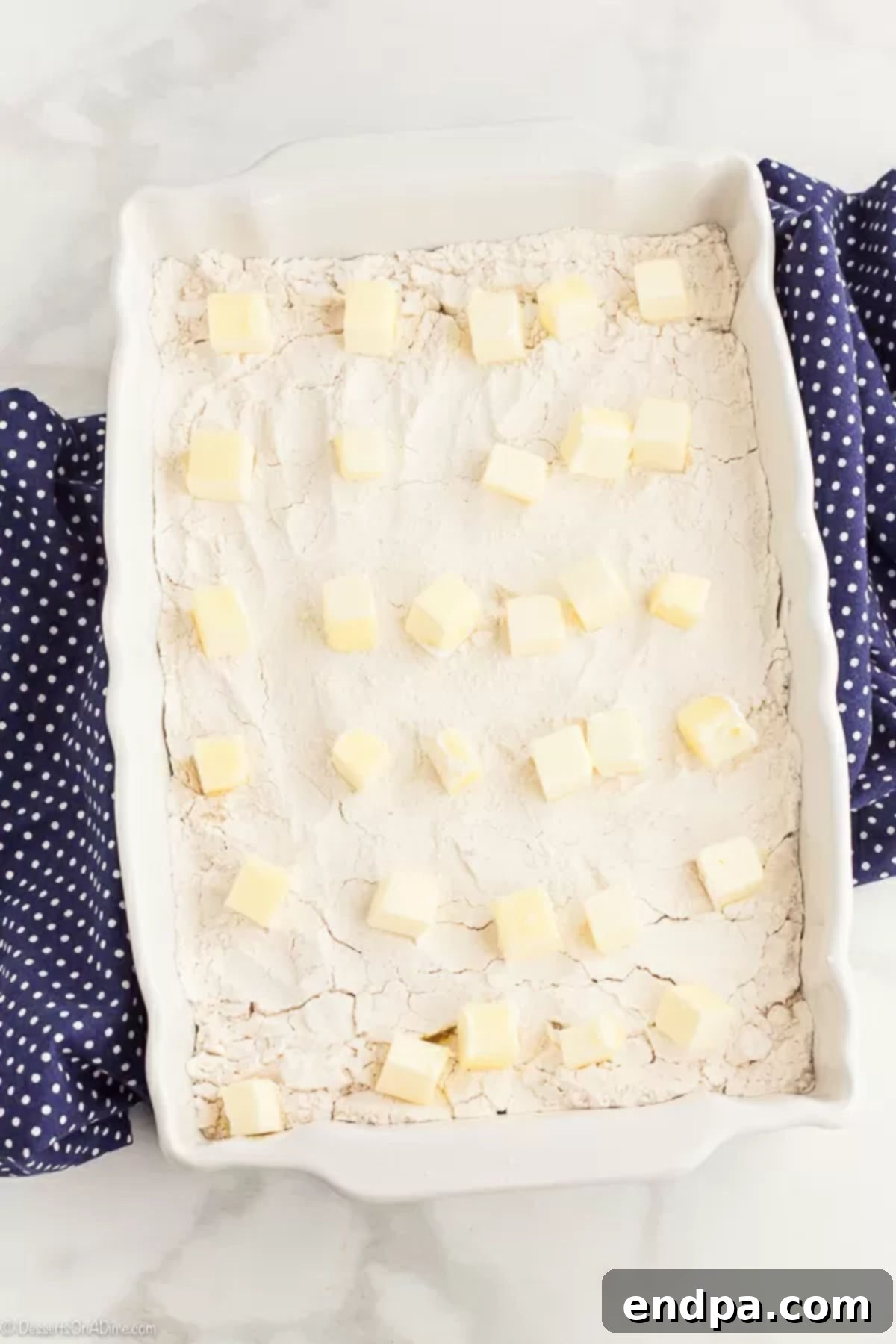 Thin slices of unsalted butter evenly layered across the dry cake mix topping in a baking dish.