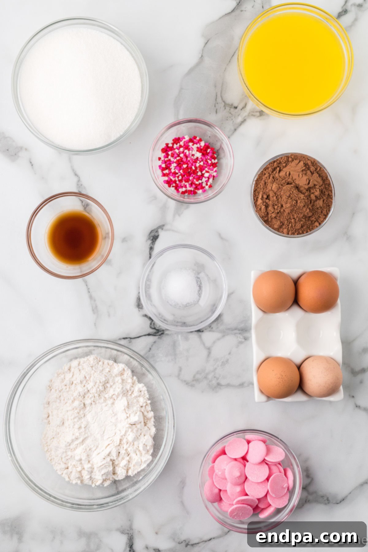 Sweetheart Brownies 3 A collection of ingredients for making heart shaped brownies: melted butter, granulated sugar, eggs, vanilla extract, unsweetened cocoa powder, pink candy melts, and multi-colored heart sprinkles.
