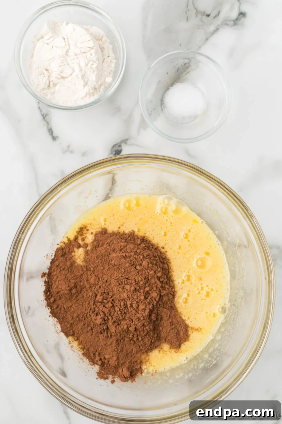 Cocoa powder being slowly whisked into the wet ingredients mixture in a large bowl.