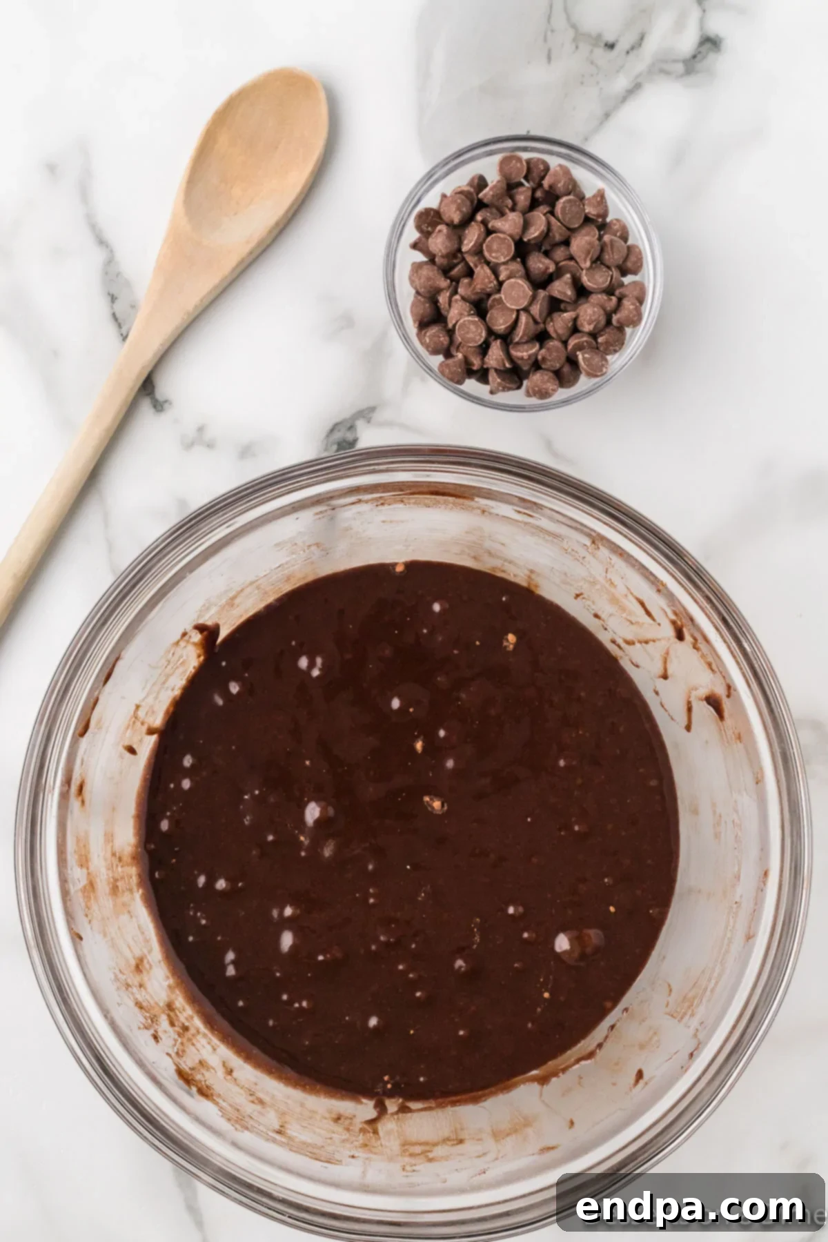 Chocolate chips being gently folded into the brownie batter in a mixing bowl.