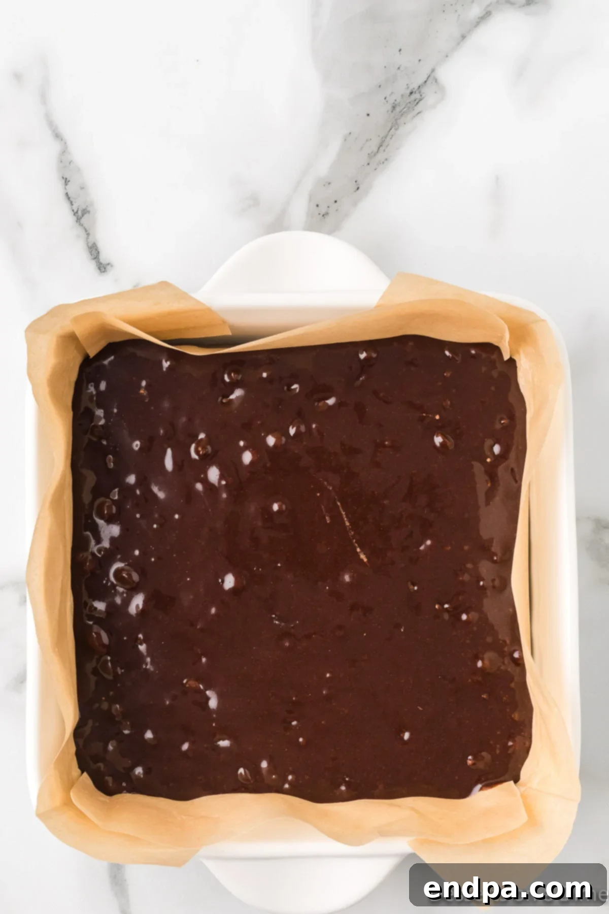 Brownie mixture being poured smoothly into the parchment-lined baking pan.