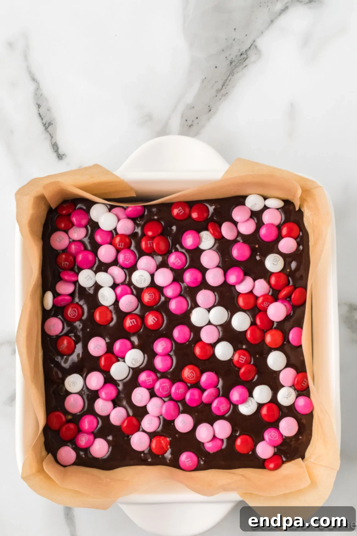 Valentine's Day M&Ms being generously sprinkled over the top of the brownie batter in the pan.