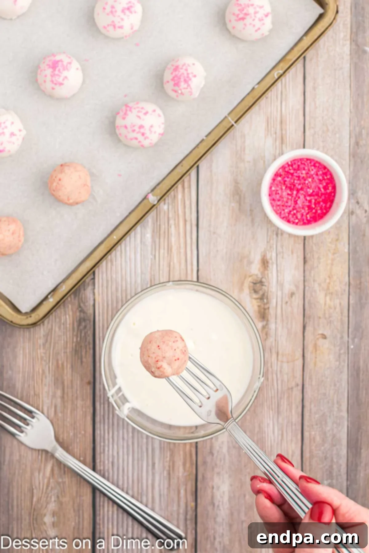 A strawberry truffle being dipped into melted white chocolate coating.