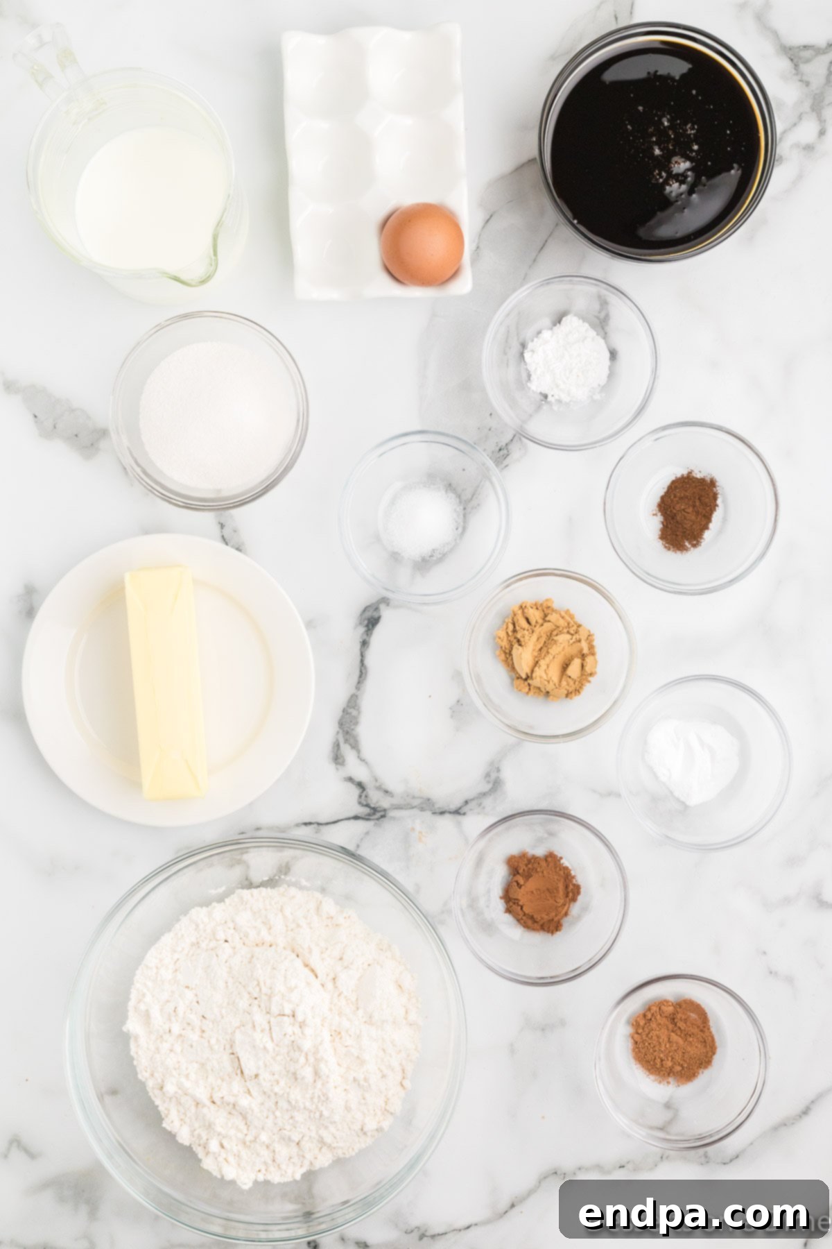 A flat lay of all the fresh ingredients required for baking a gingerbread cake, including white flour, baking powder, baking soda, salt, a variety of ground spices like ginger, cinnamon, nutmeg, and cloves, softened butter, dark molasses, granulated sugar, a large egg, and buttermilk, with additional whipped cream and powdered sugar for serving.