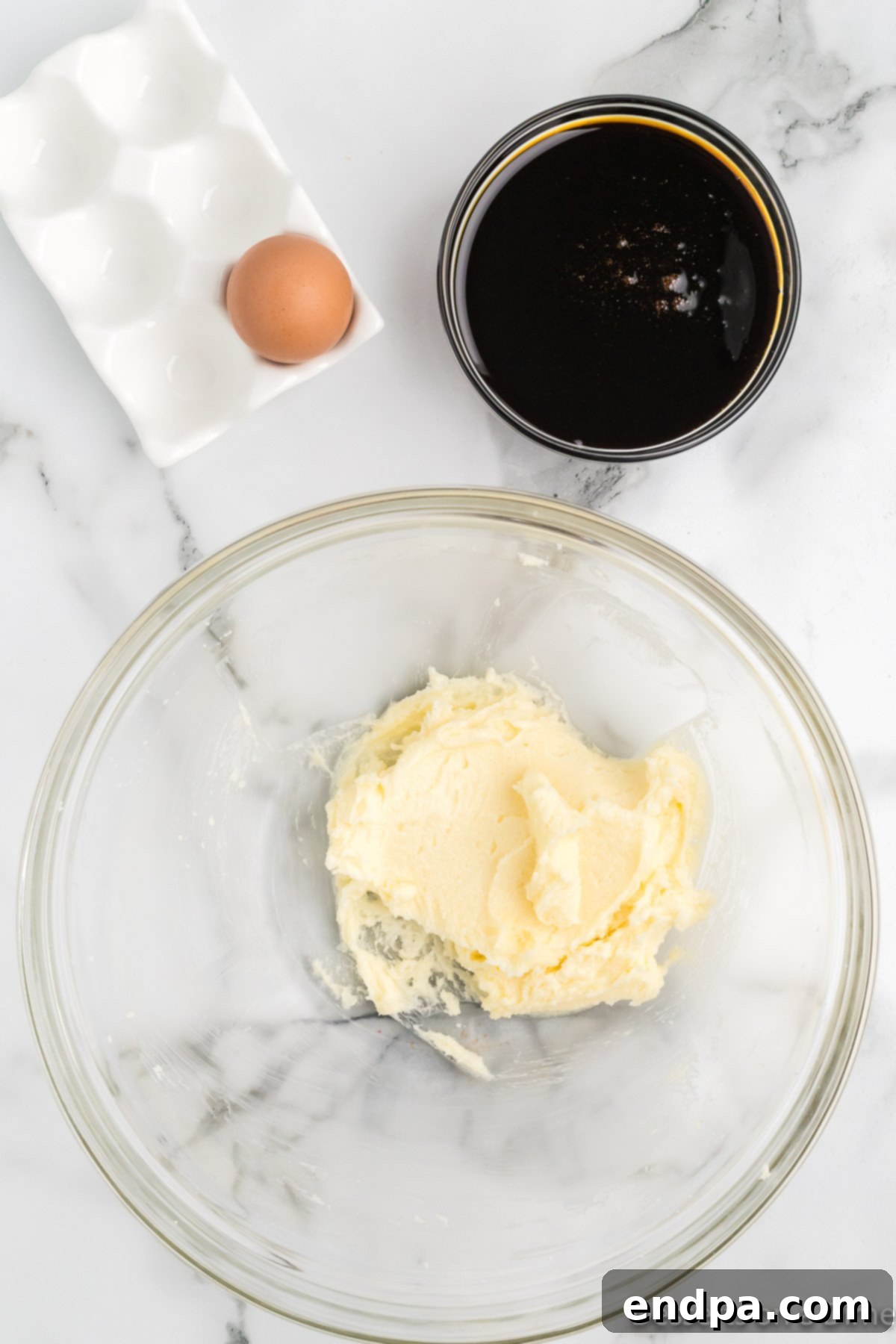 A large mixing bowl containing softened butter, granulated sugar, a raw egg, and dark molasses, with an electric mixer preparing to beat them together until creamy and well combined for the gingerbread cake batter.