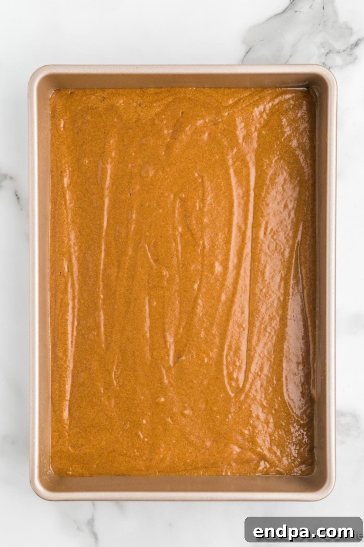 Thick, spiced gingerbread cake batter being poured evenly into a prepared 13x9 inch baking pan, ready for baking.