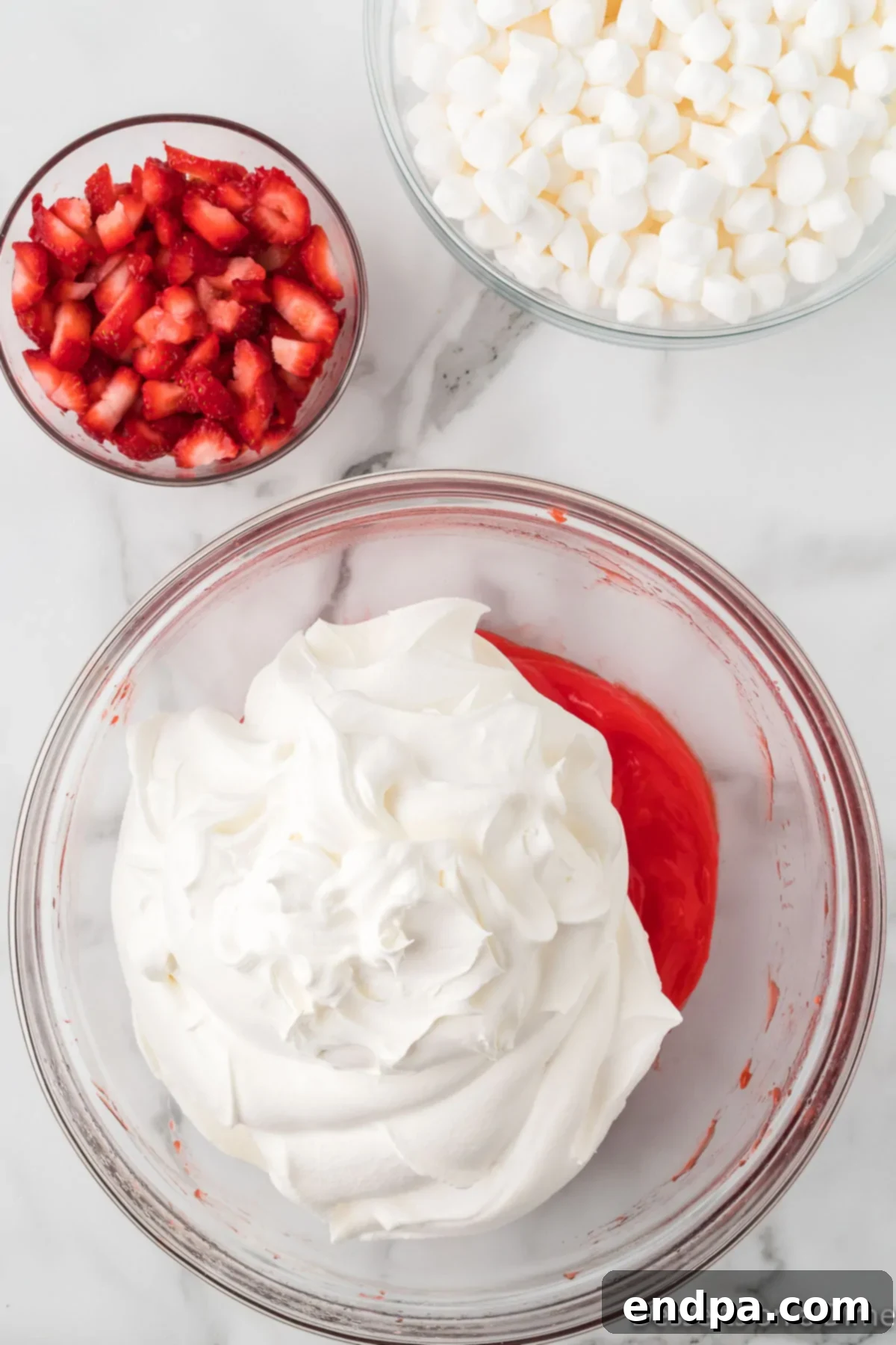 Strawberry Cloud Delight 6 Thawed whipped topping being gently folded into the creamy jello and pudding mixture in a large bowl, creating a light pink, airy base.