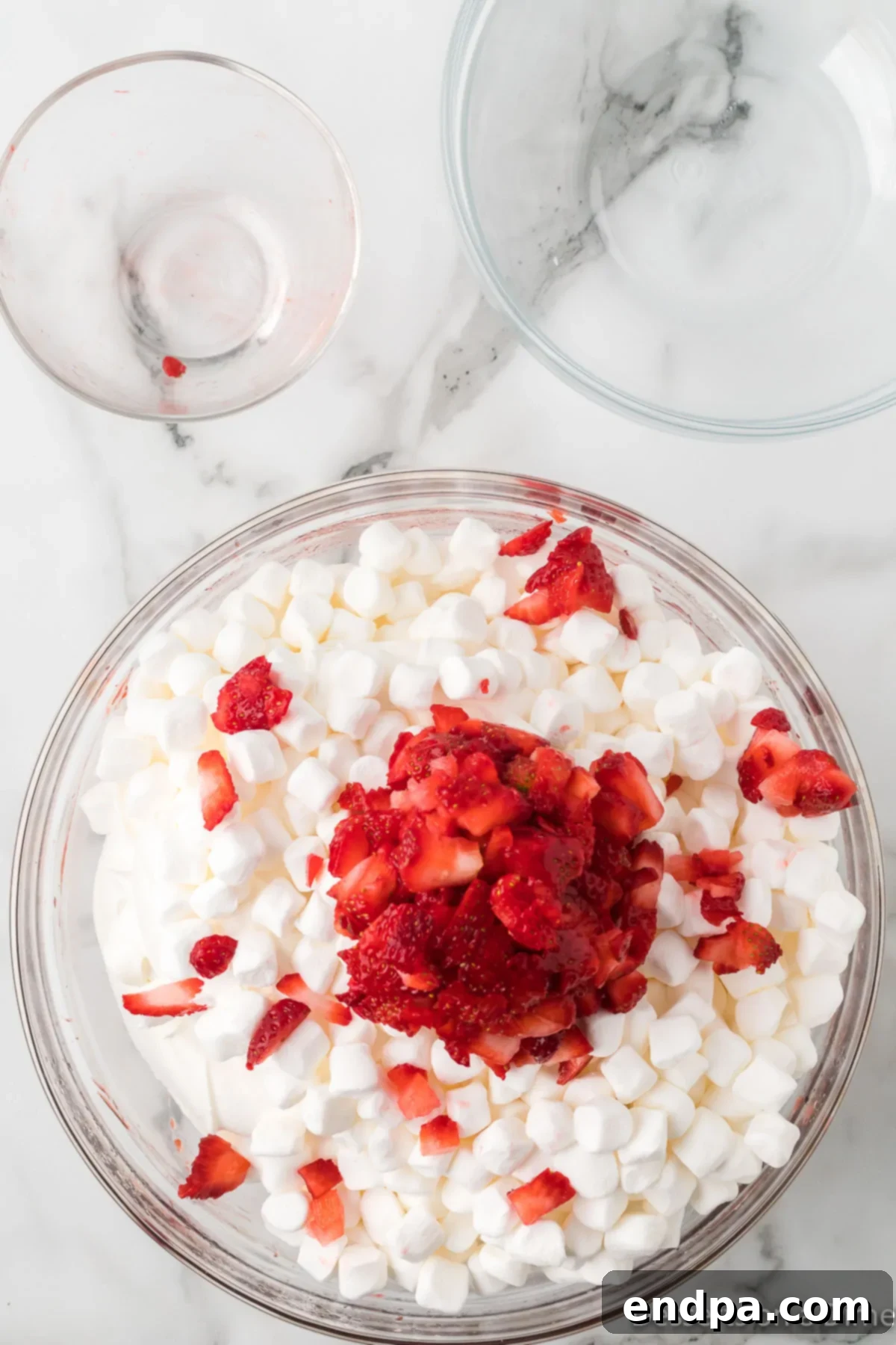 Strawberry Cloud Delight 7 Mini marshmallows and fresh, diced strawberries folded into the pink, fluffy base mixture in a large mixing bowl, showing even distribution.