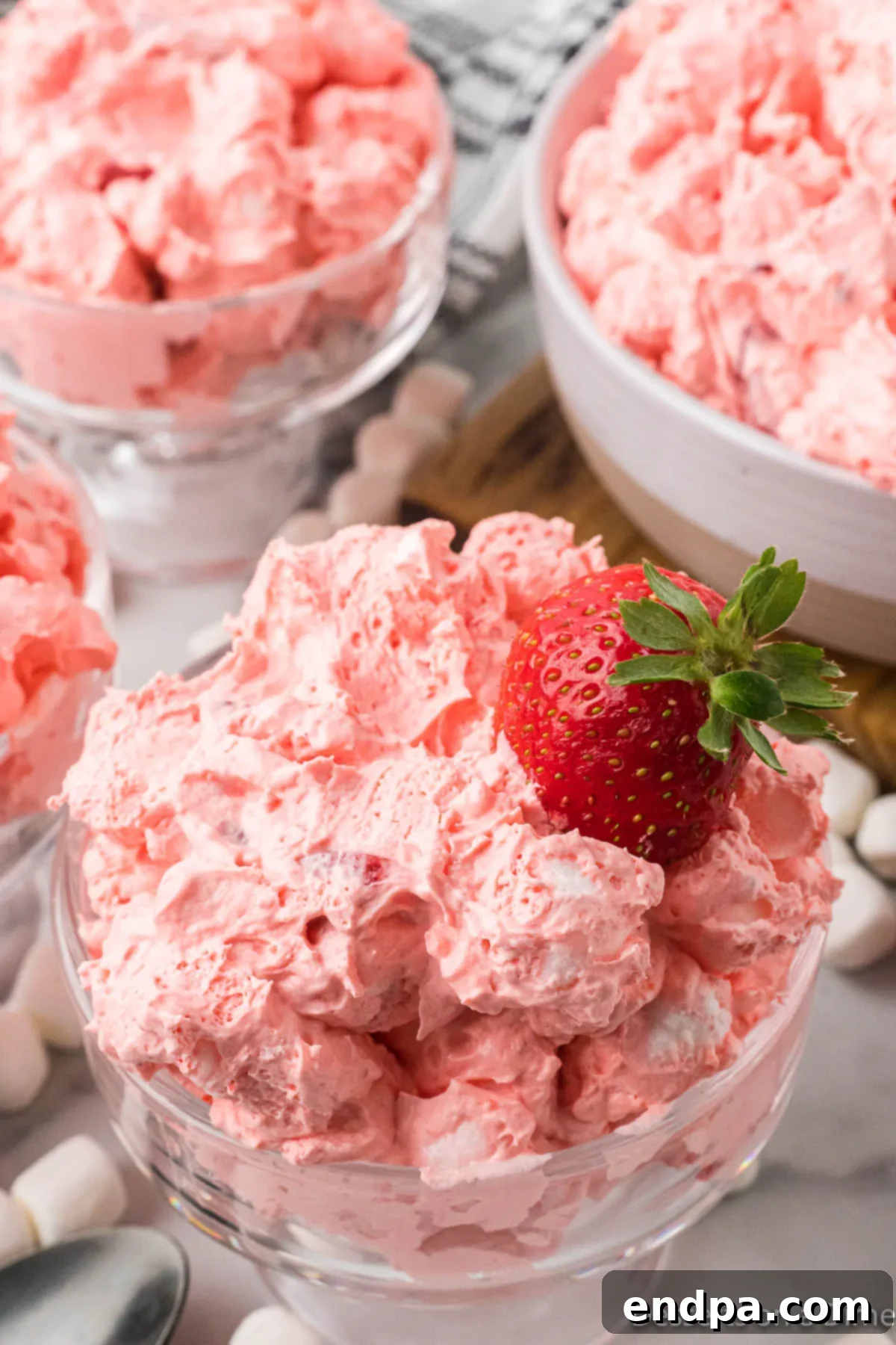 Strawberry Cloud Delight 9 A scoop of Strawberry Fluff Salad artfully placed in a clear glass serving dish, topped with a fresh whole strawberry, ready to be served.