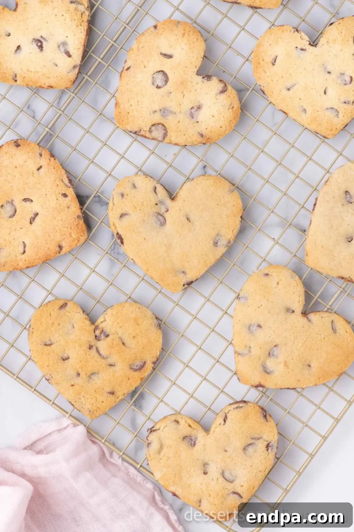 Heartfelt Chocolate Chip Bites 9 Freshly baked heart-shaped chocolate chip cookies cooling on a wire rack after being removed from the oven.