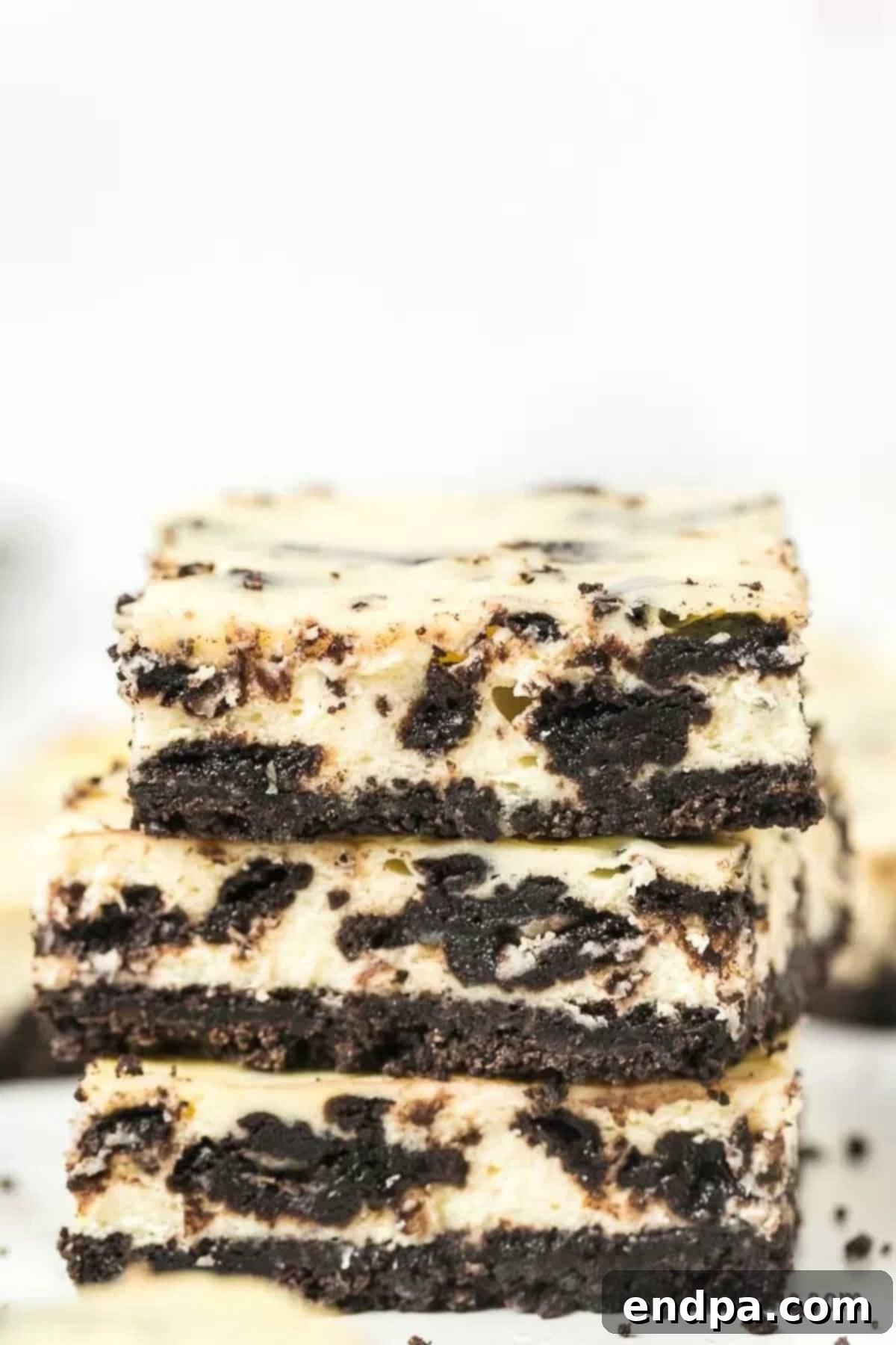 Oreo Cheesecake Bars: A delightful fusion of classic Oreo cookies and creamy cheesecake, perfect for any occasion. This easy-to-make dessert is packed with chocolatey goodness, offering a simple yet elegant treat. Enjoy these Cookies and Cream Cheesecake Bars for an unforgettable dessert. Three decadent Oreo Cheesecake Bars stacked artfully, showcasing their rich layers.