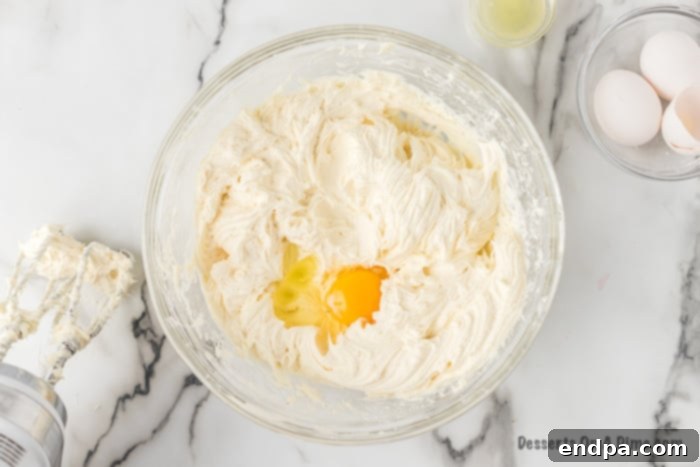 Eggs and vanilla extract being added to the cream cheese mixture.