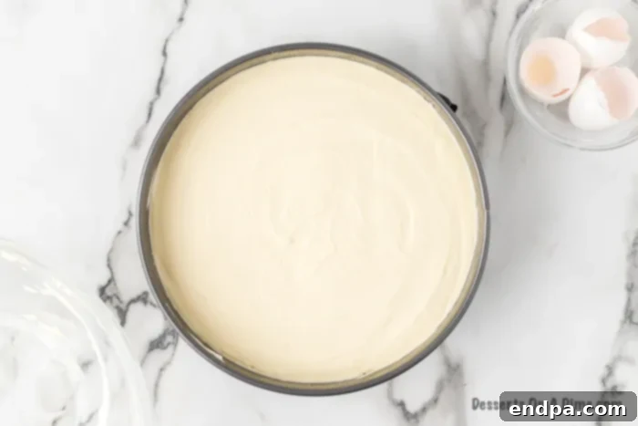 Cream cheese filling being carefully poured over the baked crust in the springform pan.
