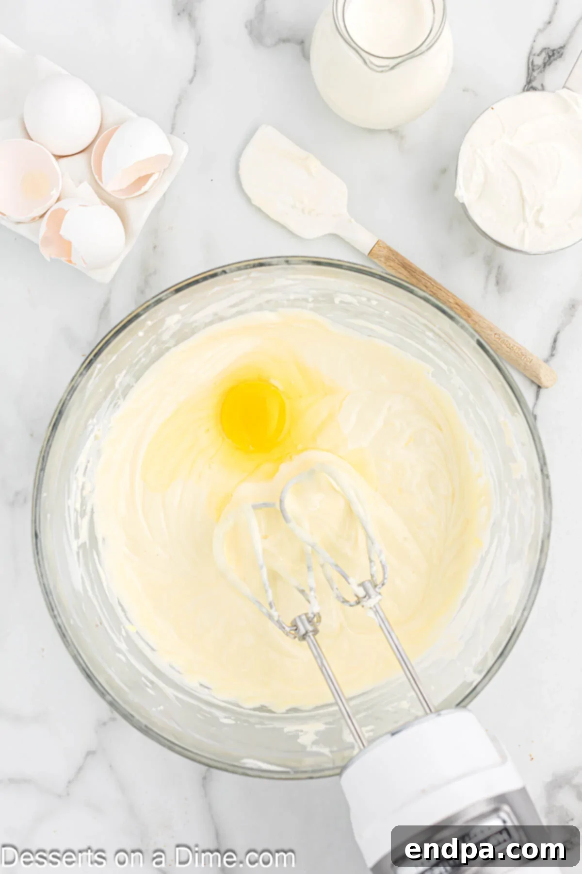 Eggs being added one at a time to the cream cheese mixture in a bowl.