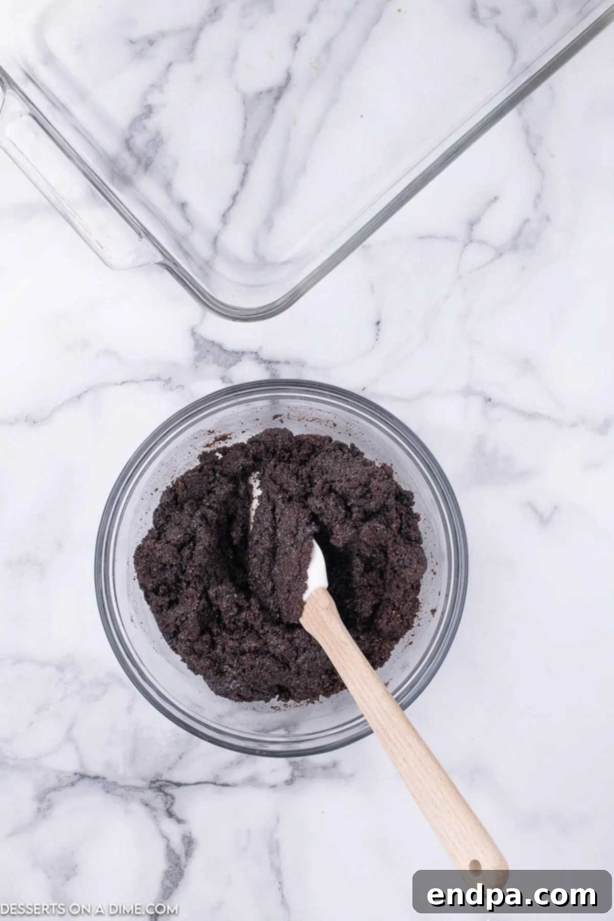 Decadent Hot Cocoa Lasagna 4 Oreo cookie crumbs combined with melted butter in a bowl, ready to be pressed into the baking dish.