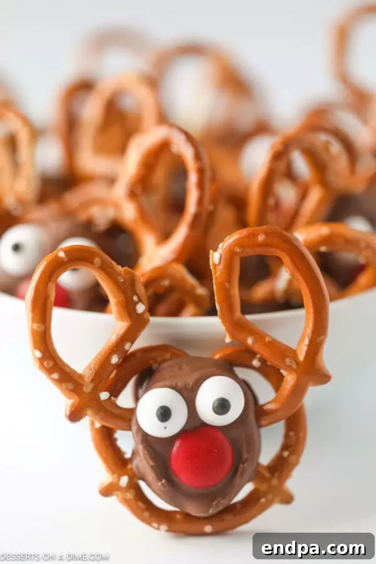 Make Easy Reindeer Pretzels with the Kids: A Fun & Festive Christmas Treat A bowl filled with festive Reindeer Pretzel treats, featuring chocolate, caramel, red M&Ms, and candy eyes on mini pretzels.