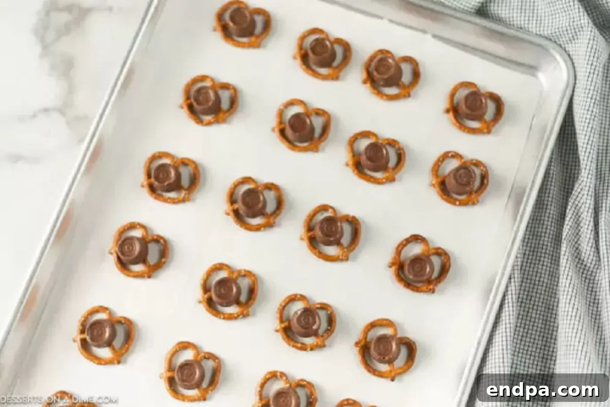 Festive Reindeer Twists 2 Mini pretzels topped with unwrapped Rolo candies arranged on a parchment-lined baking sheet, ready for the oven.