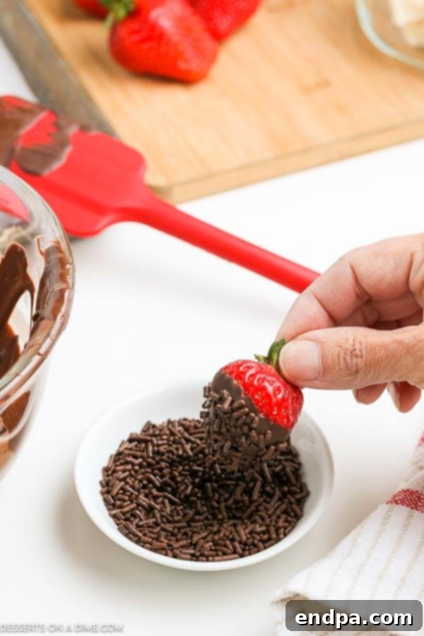A fresh strawberry being dipped into a bowl of sprinkles after being coated in melted chocolate.