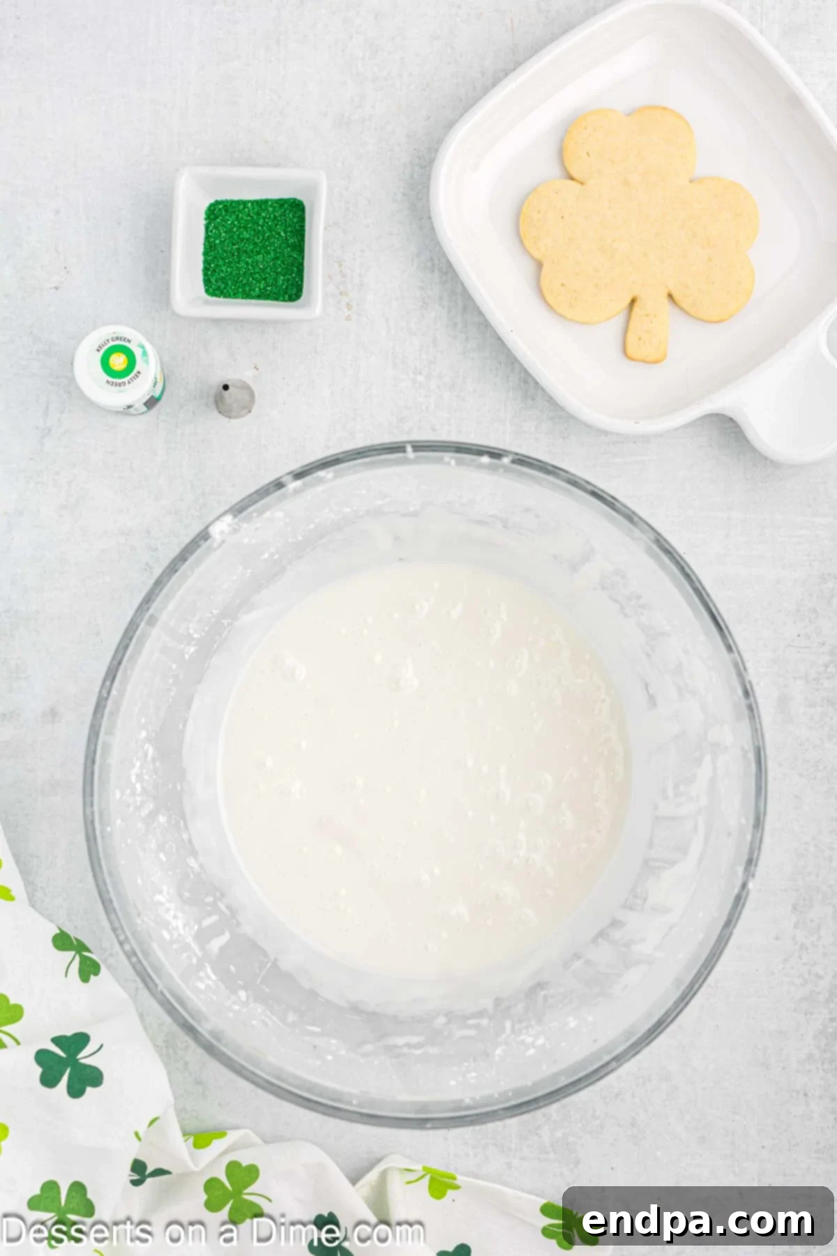 Emerald Clover Delights 11 Ingredients for green frosting, including powdered sugar, milk, light corn syrup, and vanilla extract, being mixed in a bowl with an electric mixer.