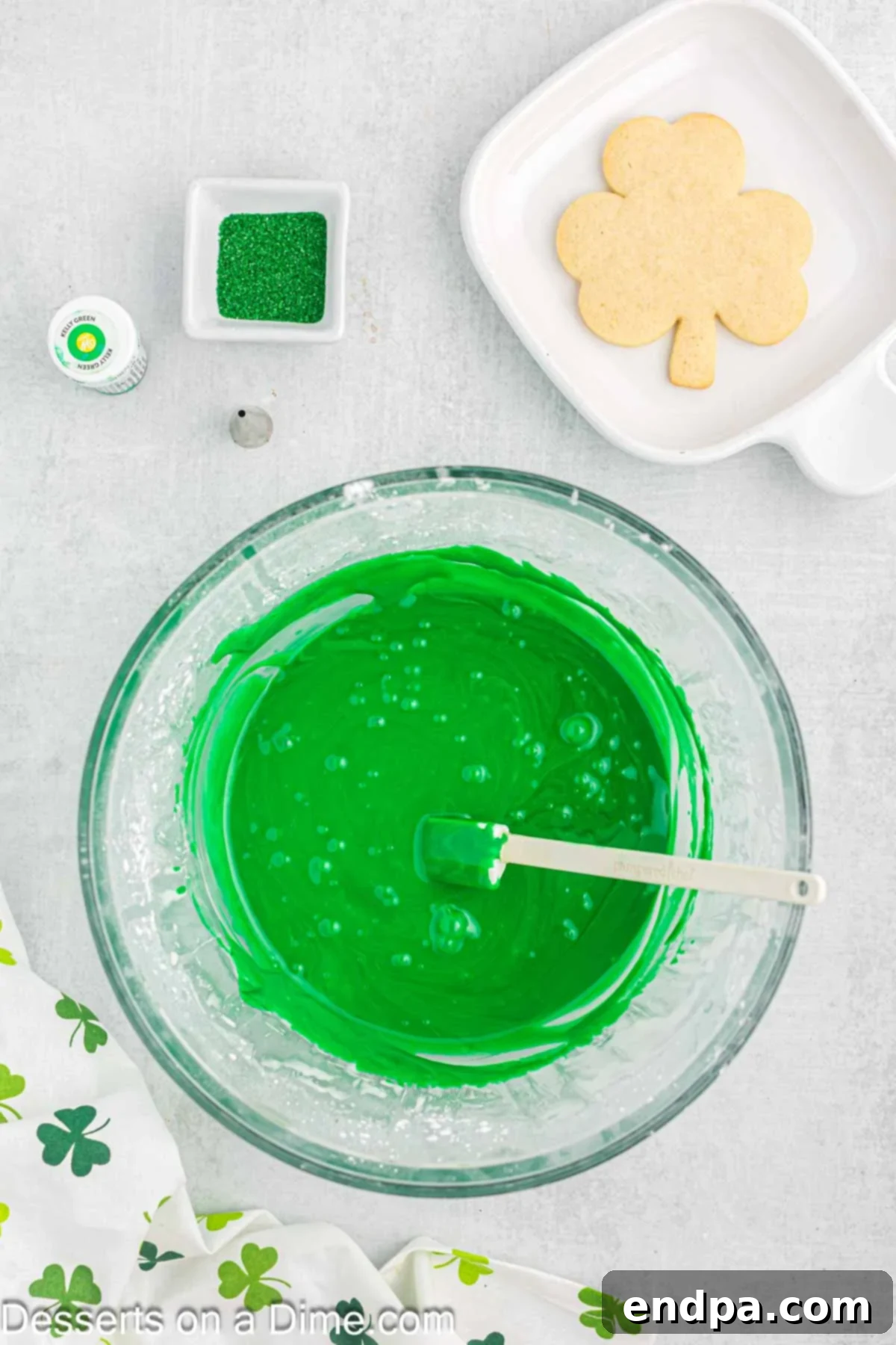 Emerald Clover Delights 12 Green gel food coloring being added to the white frosting mixture in a bowl, preparing for a vibrant St. Patrick's Day hue.