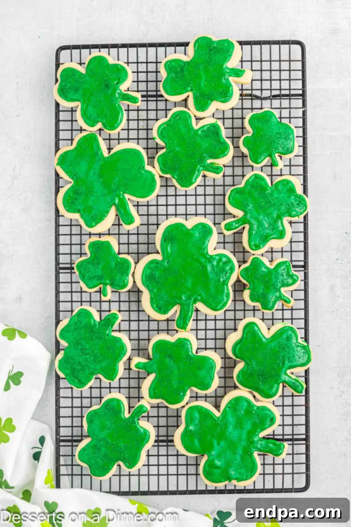 Emerald Clover Delights 14 Decorated shamrock cookies with green frosting and sprinkles drying on a wire rack to allow the frosting to harden.